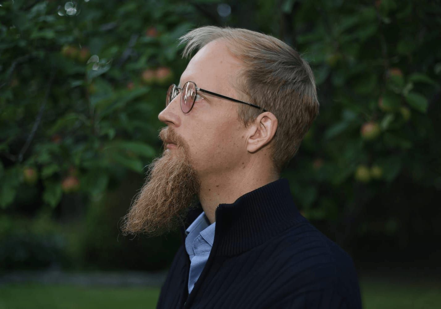 Juuso Kangas sivuprofiilissa silmälasit päässä, taustalla vihreää puutarhaa.