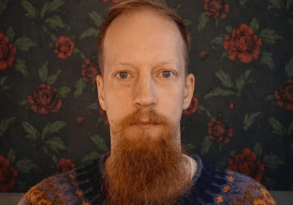 Juuso Kangas villapaidassa ruusukuvioista tapettia vasten.